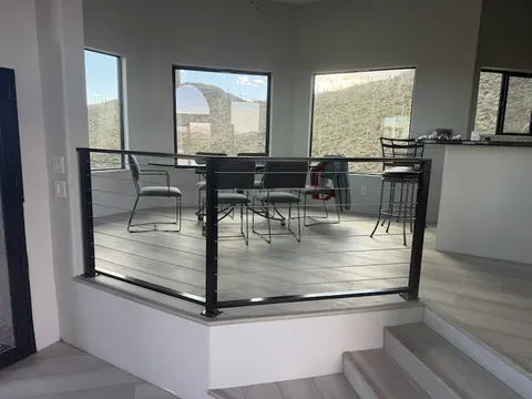 Wide view of a black steel cable railing around a raised dining platform in a desert home