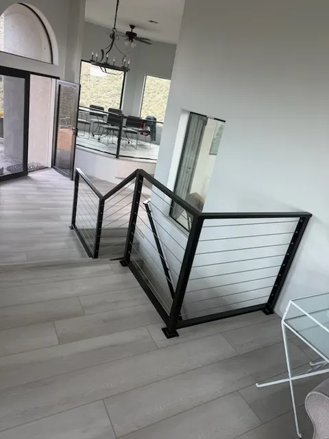 Black steel cable railing wrapping the top of an indoor stair, with a raised dining area beyond