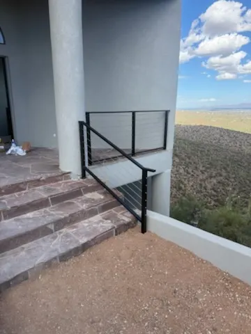 Black steel cable railing up flagstone steps to a covered porch on a desert hillside