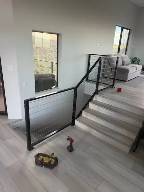 Black steel cable guardrail along an indoor stair opening beside the steps up to the living room