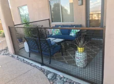 Black steel patio railing with wire grid panels and a wood top rail around a furnished patio