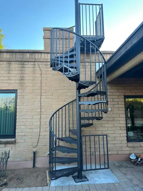 Black steel spiral staircase up to a rooftop beside a brick house