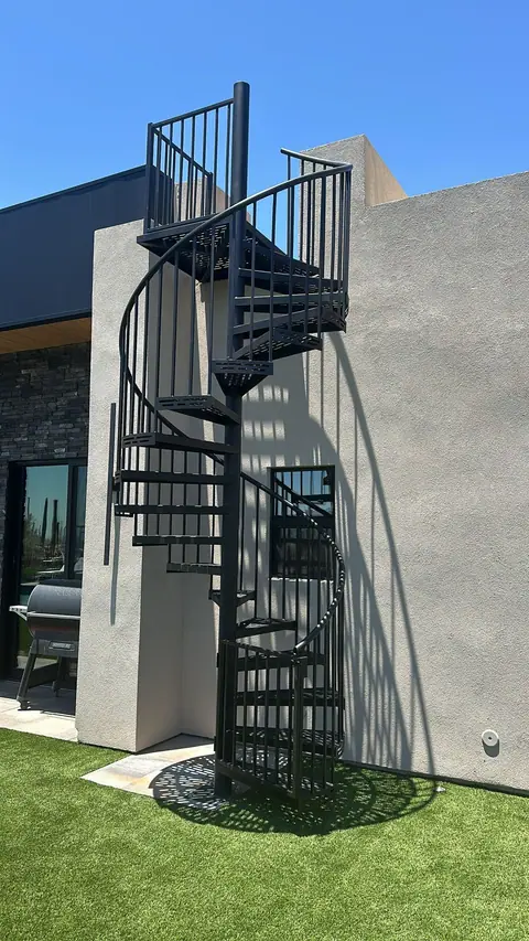 Black steel spiral staircase beside a modern stucco house