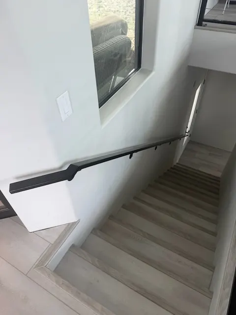 Black steel handrail mounted on brackets along the wall of an indoor stairwell