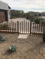 Rust finish steel bar fence with an open walkway across a gravel desert front yard
