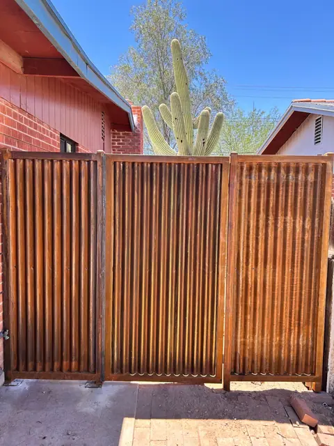Rusted corrugated steel fence and gate beside a brick house and a saguaro