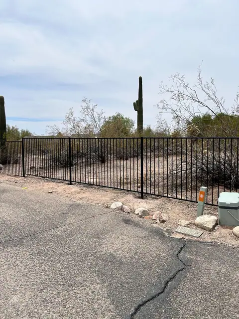 Black steel picket fence along a desert road
