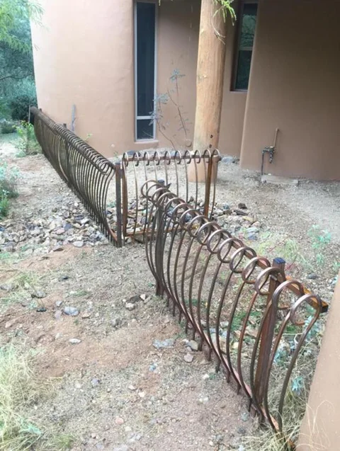 Bronze steel fence panels with curled hoop tops around the gravel bed of a stucco house