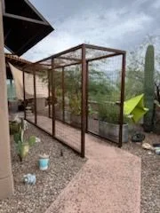 Steel frame enclosure with wire mesh walls along a garden path beside a house