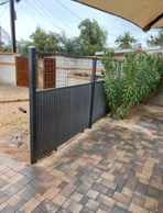 Black steel fence with a solid lower panel and a wire mesh top beside a brick paver patio under a shade sail