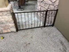 Short black iron fence between stacked stone pillars at the edge of a patio