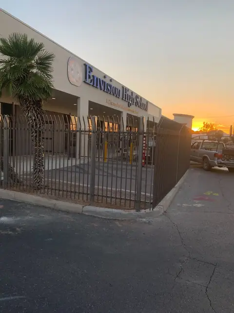 Black steel picket fence along the front walk of a school building at sunset