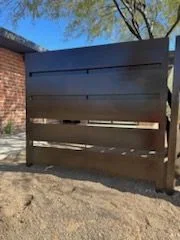 Dark horizontal slat privacy panel standing in a dirt yard by a brick house