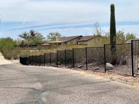 Black steel picket fence following a sloped desert road with a saguaro