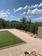 Black steel view fence along the edge of a backyard with turf and gravel, desert trees beyond