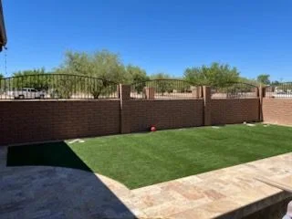 Black iron fence along the top of a block wall around a backyard lawn
