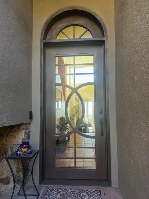 Arched iron entry door with glass, a circle pattern and a fan transom in a stucco entry