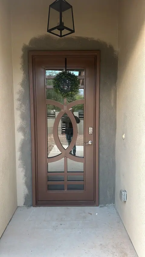 Bronze iron entry door with glass and a linked circle pattern in a recessed stucco entry