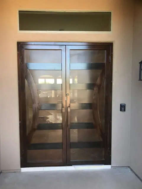 Double bronze doors with clear panels behind curved and horizontal bars, under a transom window