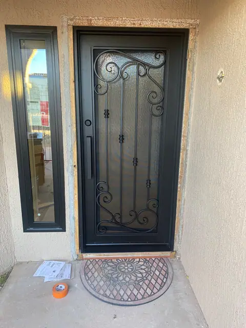 Black iron entry door with glass and scrollwork beside a matching sidelight