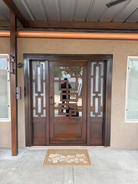 Bronze iron entry door with glass and geometric sidelights under a steel porch cover