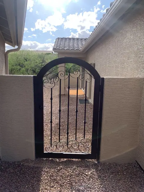 Arched black walk gate with scrollwork in a stucco courtyard wall