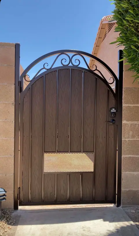 Arched brown walk gate with a scroll top, a mesh window and a keypad lock between block walls