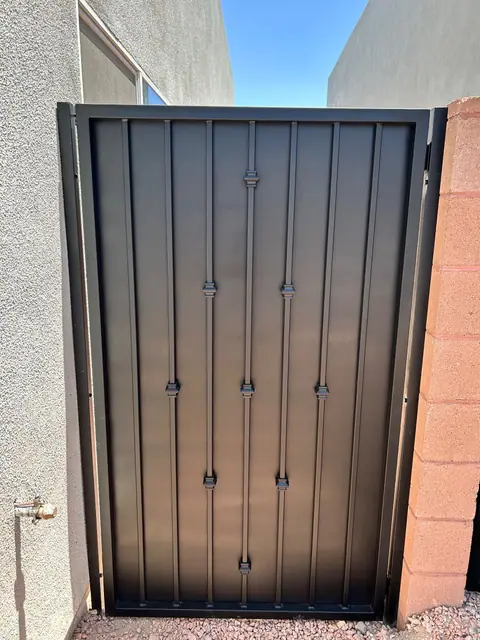 Black walk gate with bars and collars between a stucco wall and a brick wall