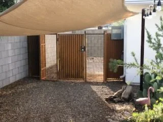 Rusted corrugated steel gate with wire mesh panels under a shade sail