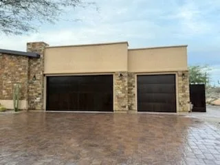 Two dark garage doors and a matching side gate on a stone and stucco house over a paver drive