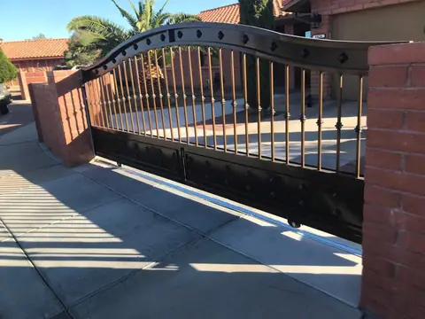 Arched rolling gate with bars and diamond accents beside a brick pillar