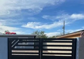 Black steel double driveway gate with horizontal slats and a diagonal brace between stucco walls