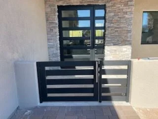 Black horizontal slat gate and matching fence panel in front of a stone and stucco entry with glass doors