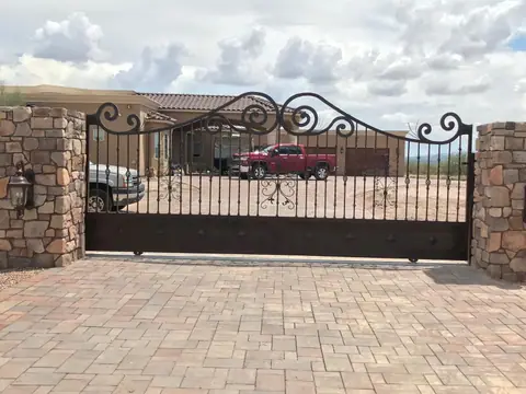 Scroll top drive gate between stone pillars over a paver driveway