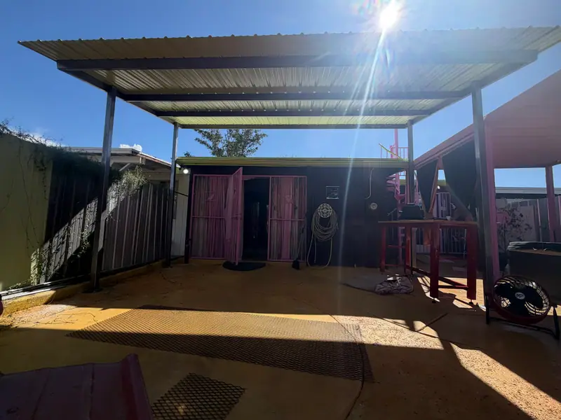 Steel patio cover with a corrugated metal roof on square posts shading a backyard