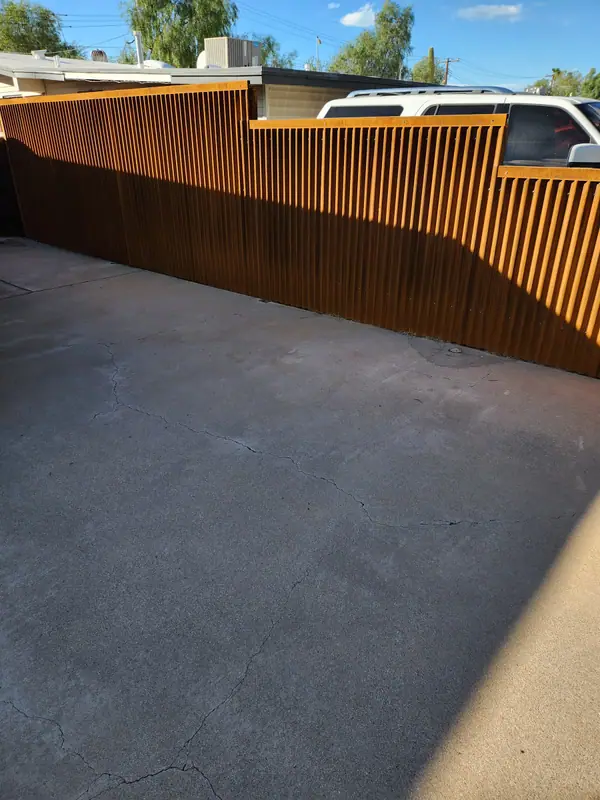 Rusted corrugated steel fence with a raked top running along a driveway