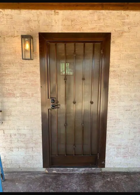Bronze security door with vertical bars and collars on a painted brick wall beside a lantern