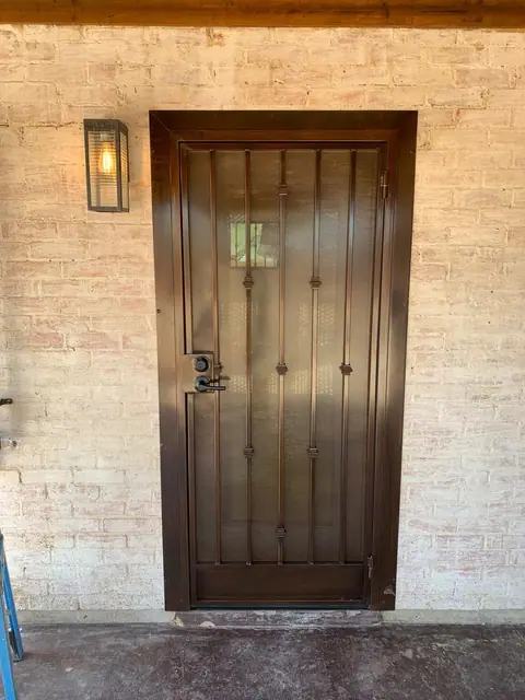 Bronze security door with bars and collars on painted brick, seen straight on