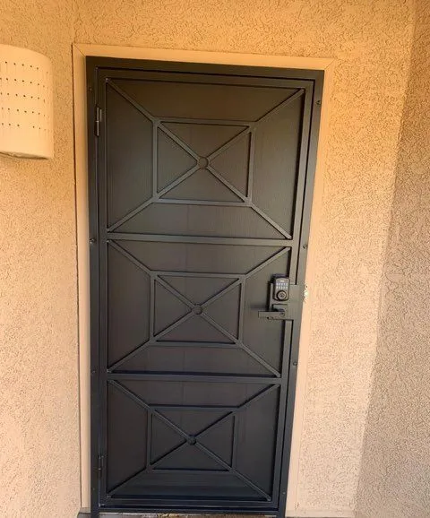 Matte black security door with an X and box pattern over screen and a keypad lock, at a stucco entry