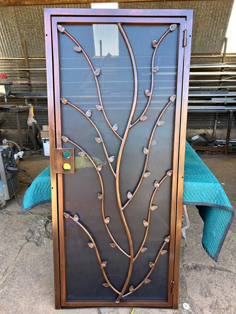 Security door with a cut steel tree branch and leaves in copper over screen, in the shop