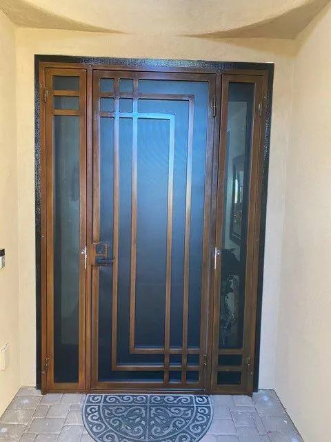 Copper finish security door with a geometric line pattern and matching screened sidelights in a curved stucco entry