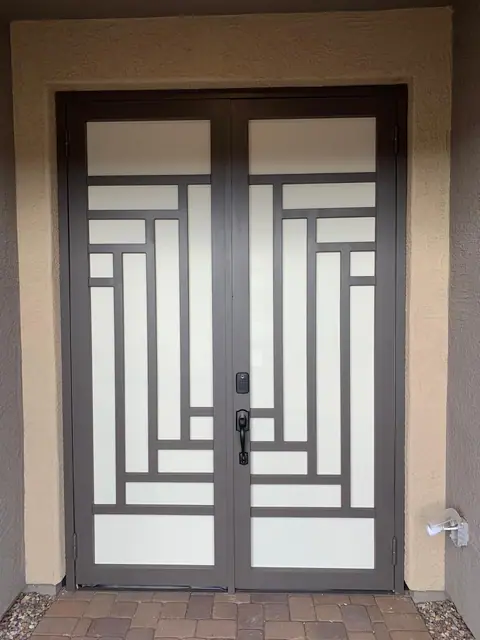 Double security doors with a stepped line pattern over white screen at a paver entry