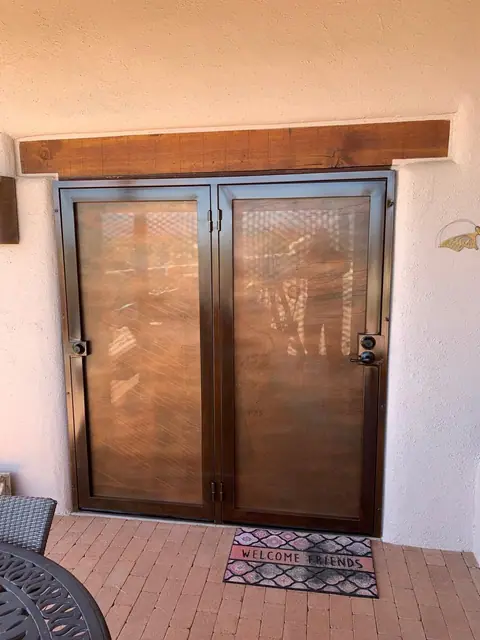 Double security doors with perforated screen panels in bronze under a wood beam