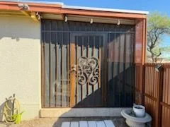 Rust brown steel security door with a scroll center set in a barred side entry