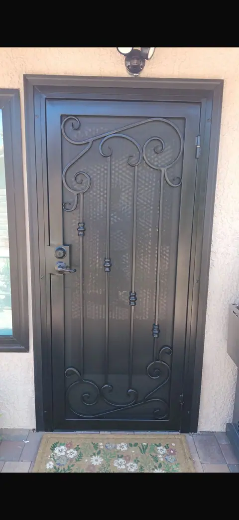 Black security door with a scrollwork top over mesh at a stucco entry