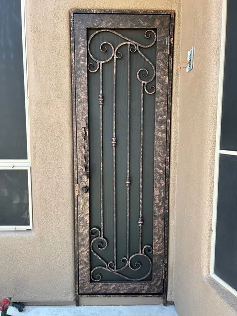 Security door with scrollwork in a copper vein finish at a stucco entry
