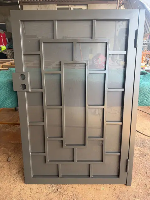 Security door with an offset rectangle pattern over screen, finished in gray and standing in the shop