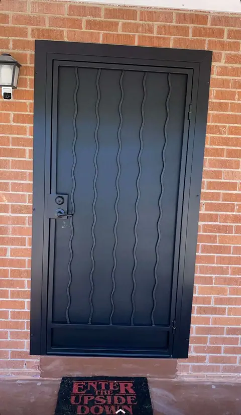 Black security door with wavy vertical bars on a red brick house