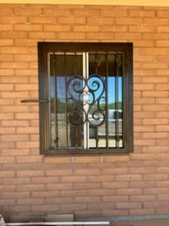 Black steel window guard with a scroll center on a brick wall
