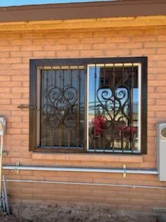 Black steel window guard with scroll panels over a wide window on a brick house